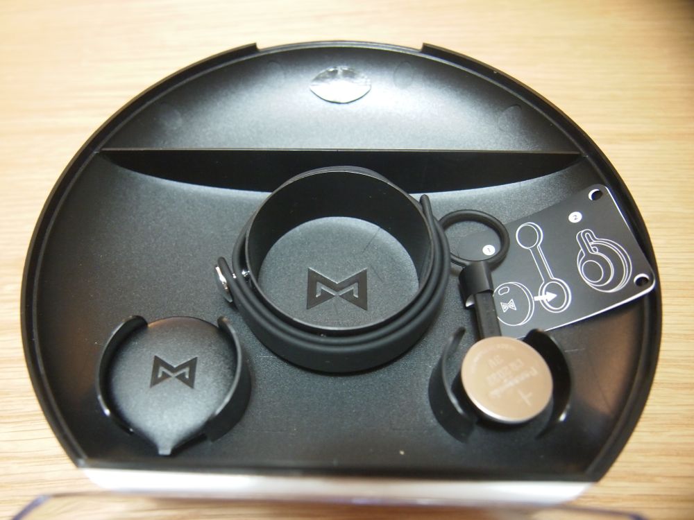 bottom left is a pick tool to open the device for battery replacement; at the center is the wrist band and on the right is a magnetic clip and a battery.