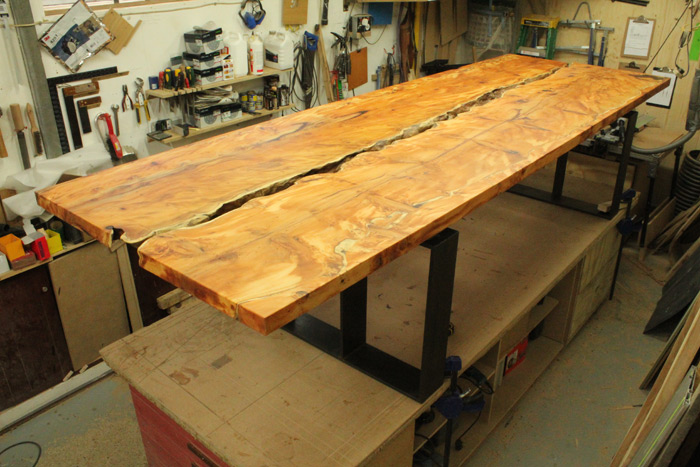 The picture shows the heavy black waxed steel legs being fitted in the workshop. The oiling has enhanced the rich natural colour of the yew which will darken with age.