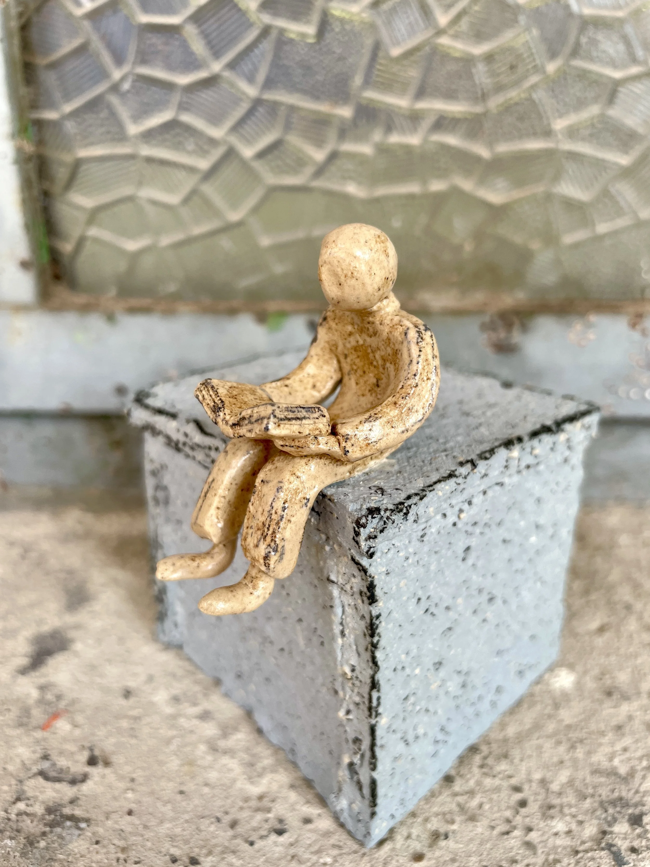 ceramic sculpture of a small figure reading a book on a pedestal