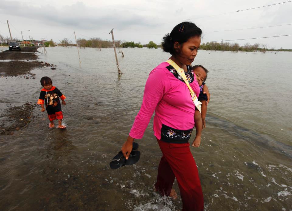 A mother carries her baby on a street flooded with sea water in Mayangan village in Subang, Indonesia. REUTERS/Beawiharta