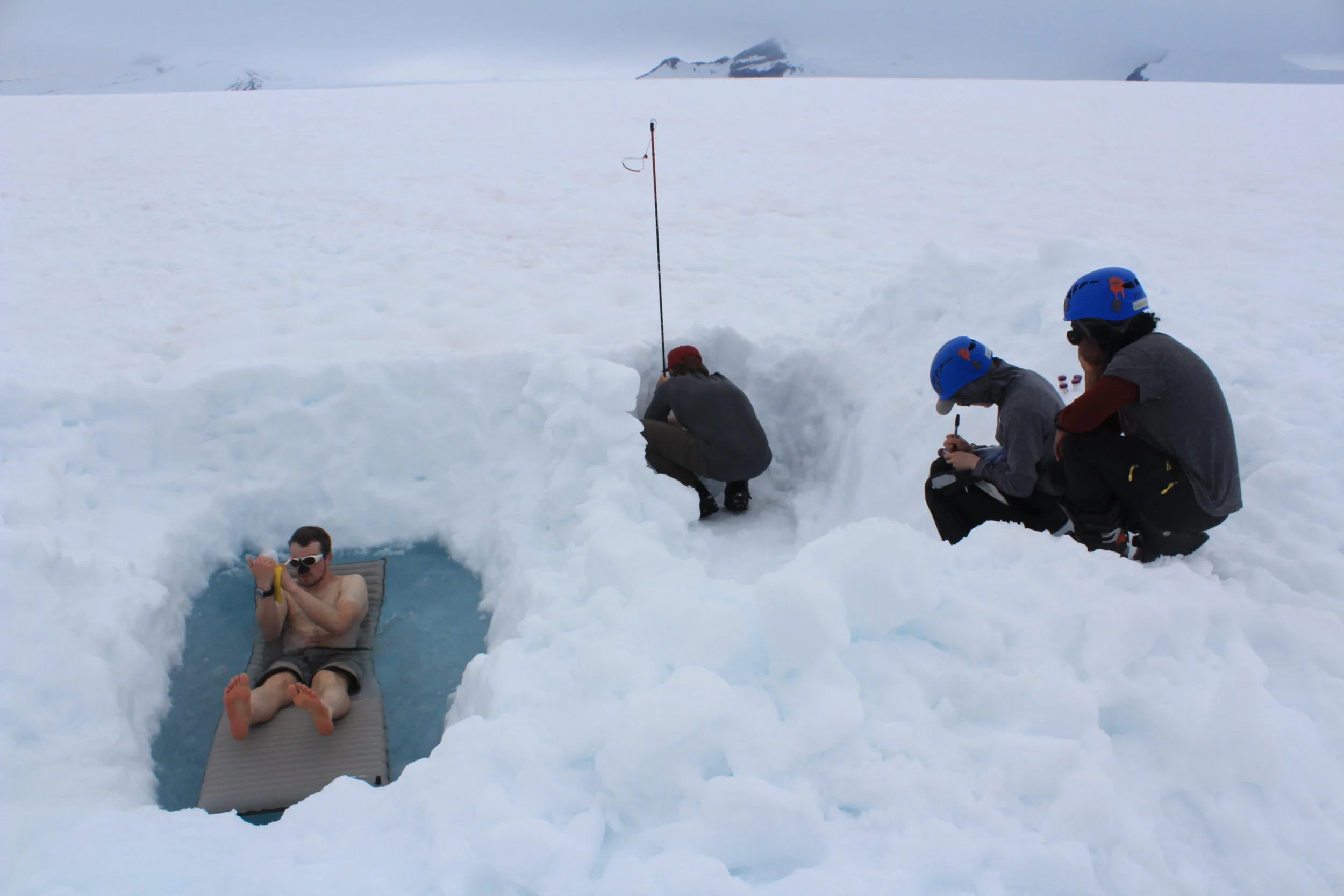 Alex Ihle floats on his therm-a-rest in the pool while recording data in the group field notebook. JJ Graham takes a snow sample form the pit while Jane Hamel labels sample bottles and Chelly Johnson organizes the samples. Photo credit: Jay Ach.