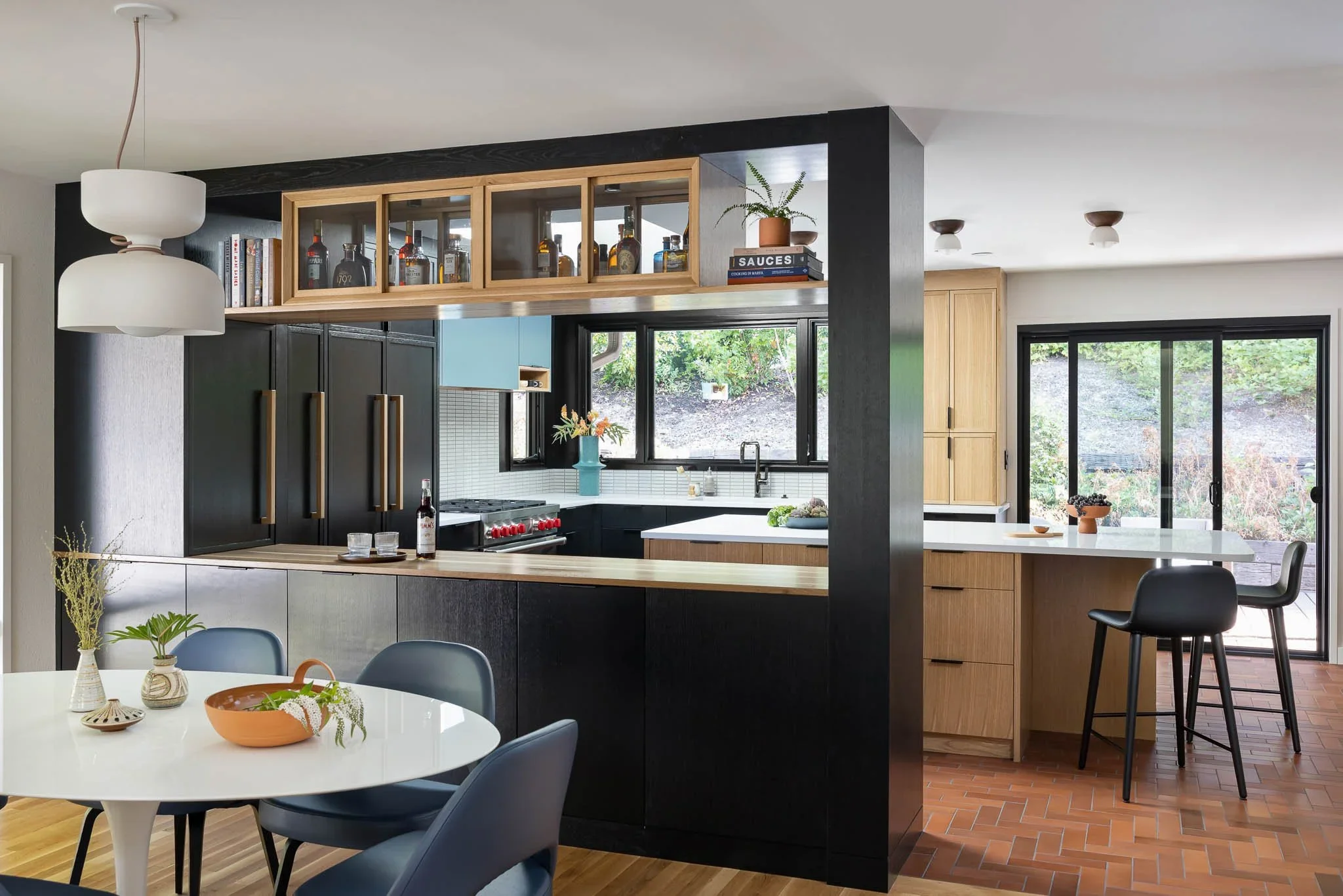 Modern kitchen with black and wood cabinetry, large island, and sliding glass door with outdoor view.