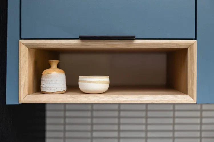 Close-up of a built-in wooden shelf with two ceramic vases on it, mounted inside a blue cabinet.