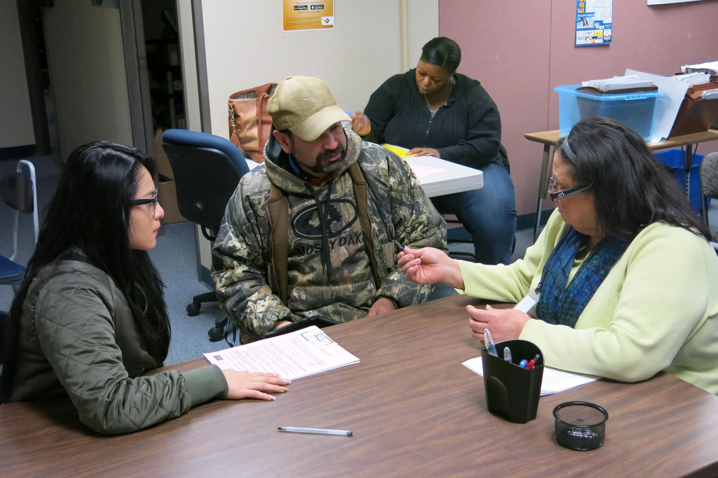Yohana Gomez, left, and her stepdad, Rogelio Romo, fill out forms in Barb Wunsch's office. Gomez started the year in Hickman Mills, moved to Kansas City, Kansas, to live with a relative, before returning to the district. CREDIT ELLE MOXLEY