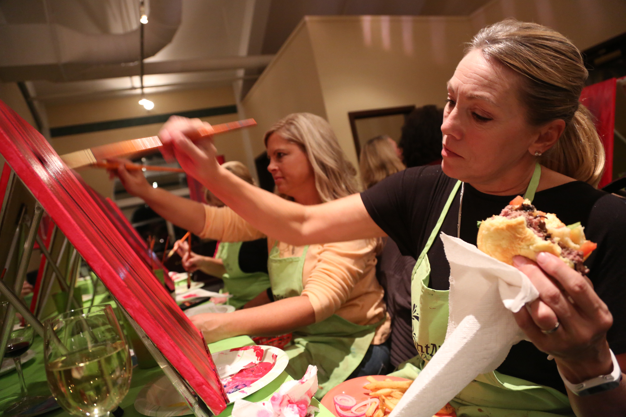 Naomi Munkittrick from Dillsburg paints on her canvas with a brush and holds her burger in the other hand during Paint Nite at Bogey Macaws American Grille in York Township. Munkittrick admitted she was starving and said, "When you are a mom, you learn to multitask." Photo by Sonya Paclob