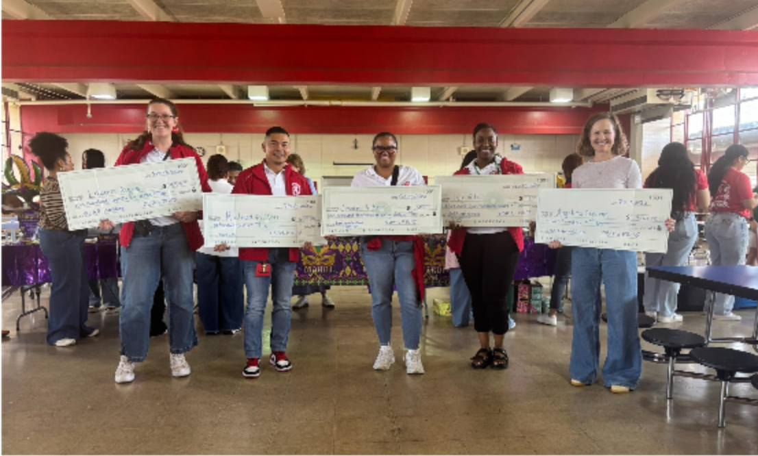 Five FBMS teachers and staff in the school cafeteria holding oversized PTO teacher grant checks