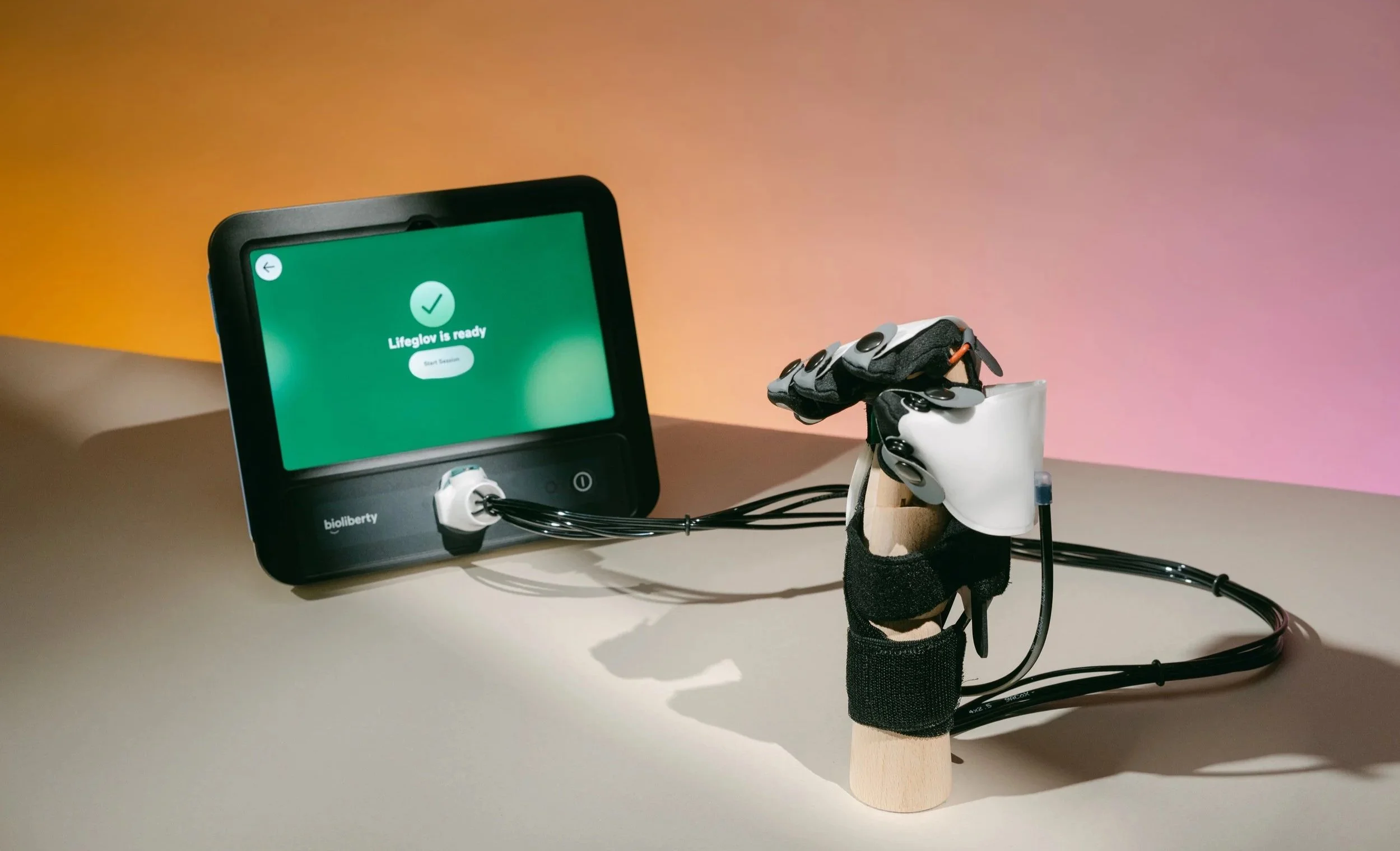 A robotic hand attached to a wooden base, connected to a digital monitor displaying a message 'LifeGlov is ready,' with a colorful gradient background.