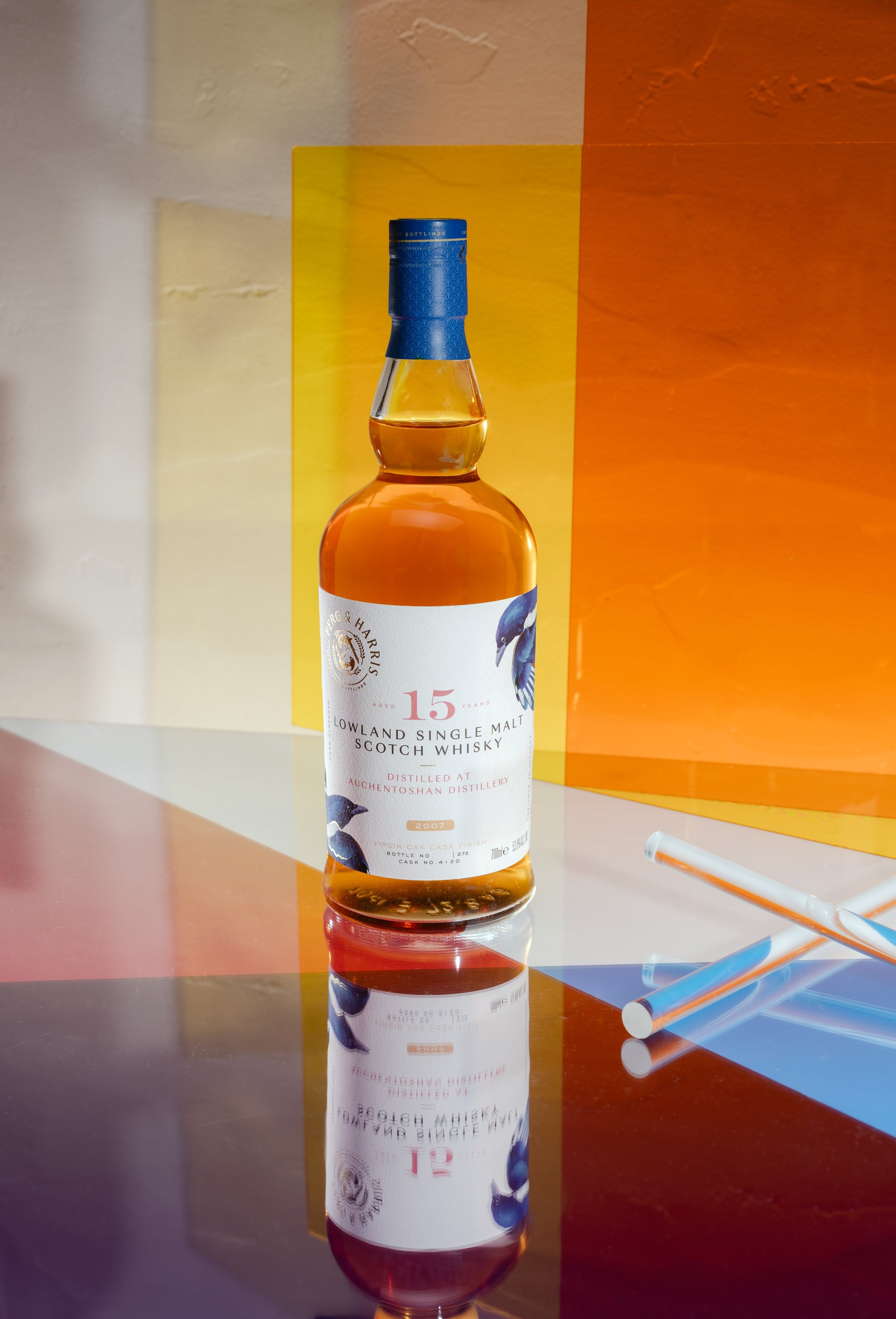 A bottle of 15-year-old Lowland single malt Scotch whisky on a reflective surface with colorful geometric background.