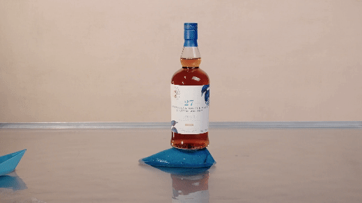 Bottle of rosé wine balanced on a blue bag on a light-colored surface with a plain background.
