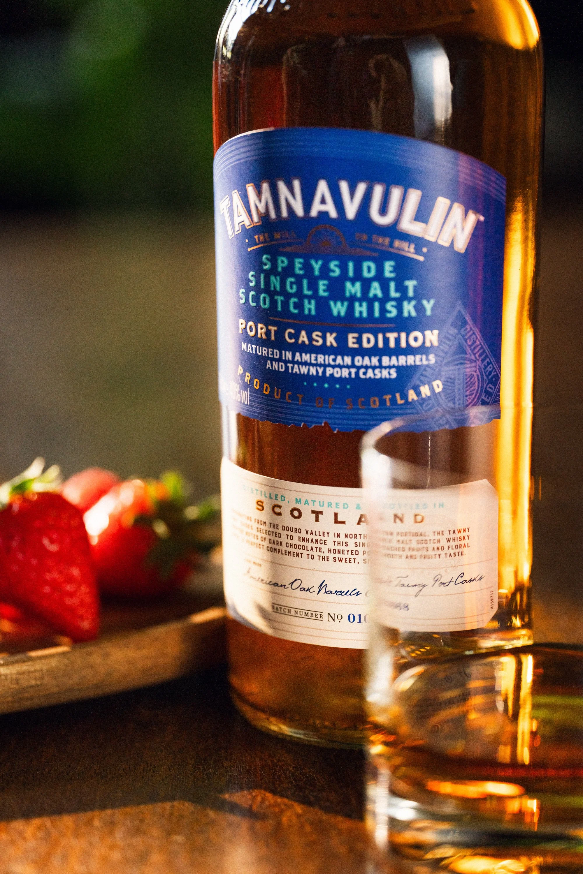 Bottle of Tamnavulin Speyside single malt Scotch whisky with a glass in front and strawberries in the background.