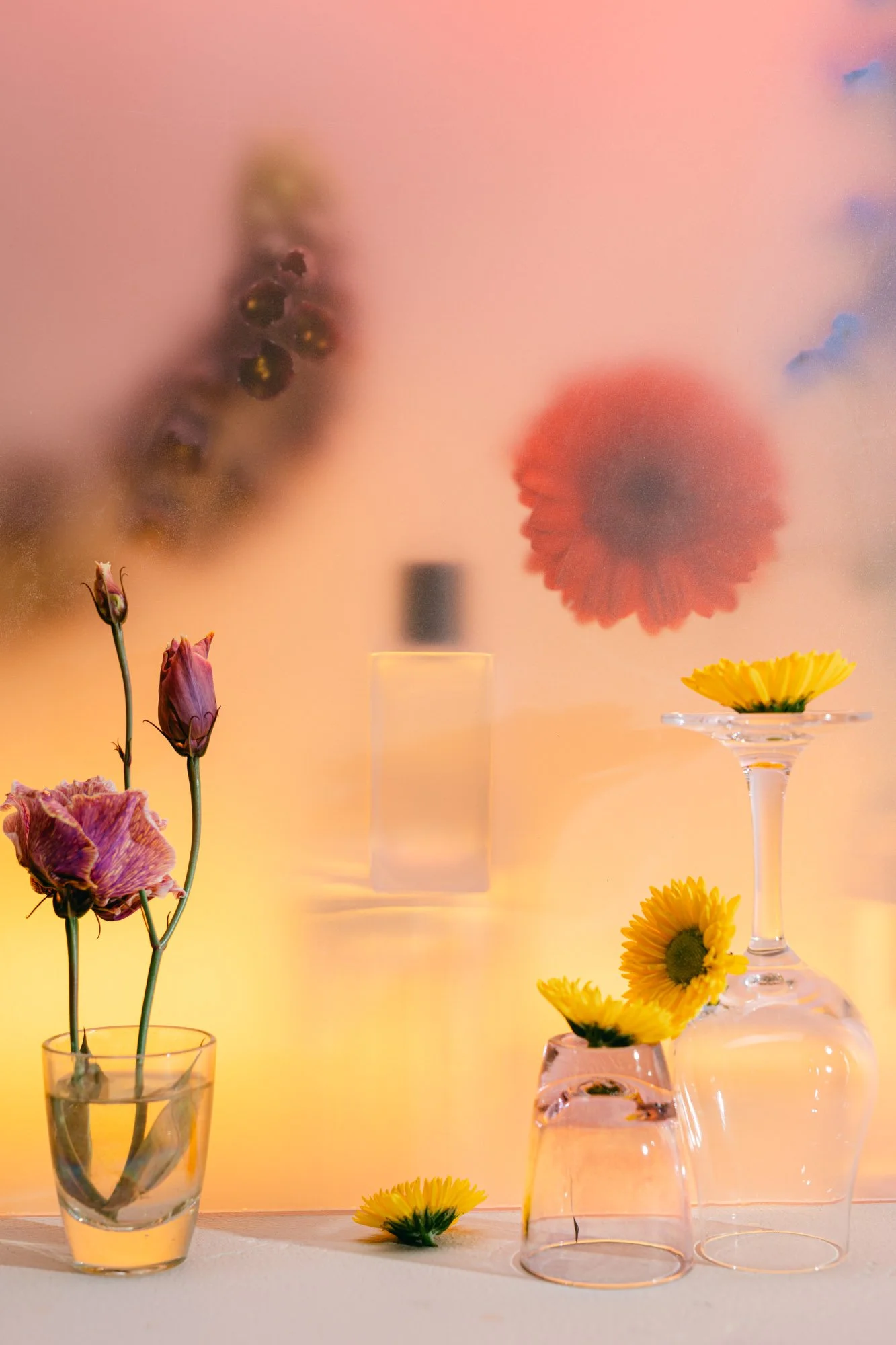 Several vases with flowers, including pink, yellow, and orange blooms, arranged on a table with a colorful, blurred background.