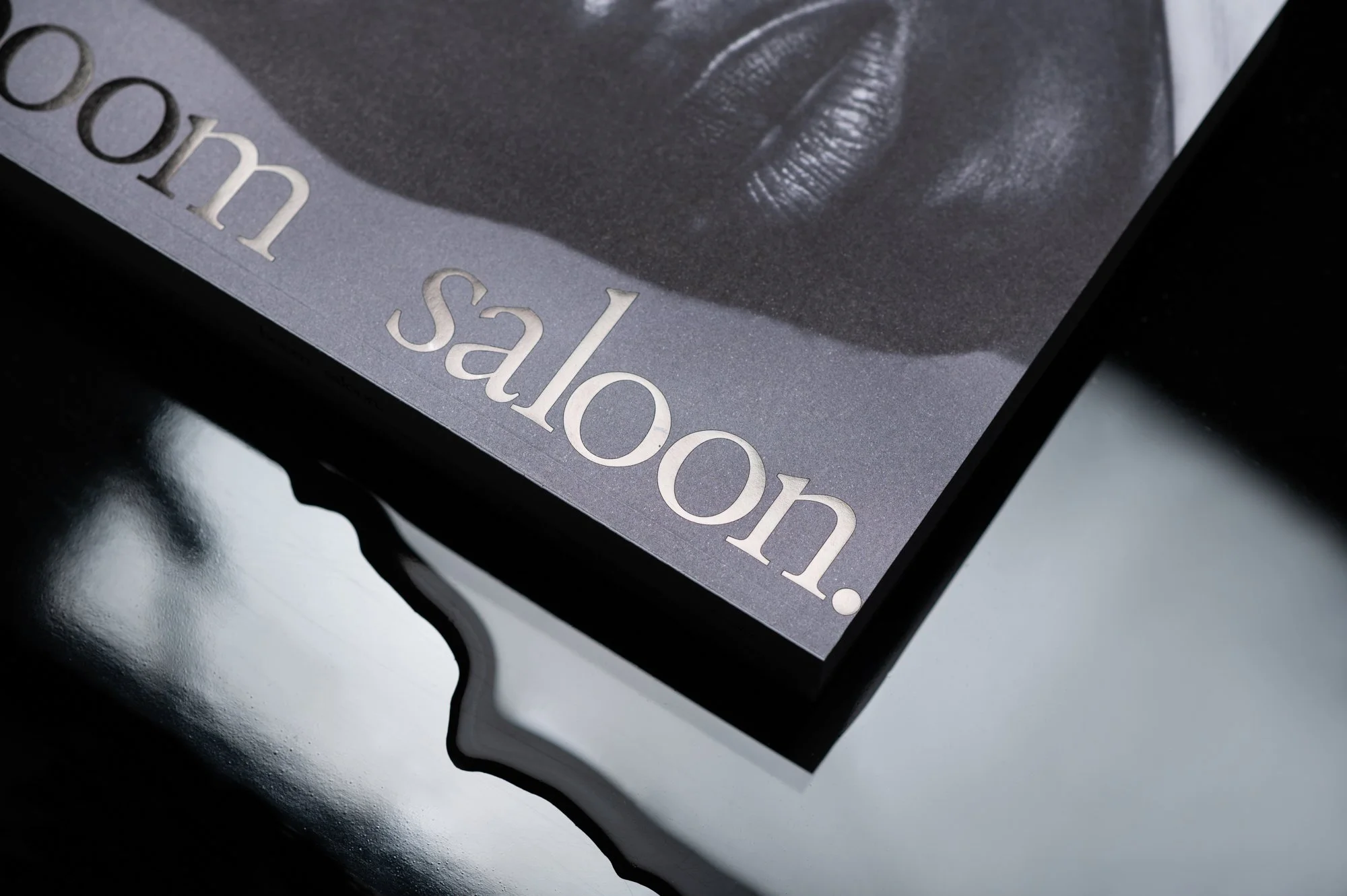 Close-up of a book titled 'salon' with a black-and-white image of a person's lips on the cover, resting on a reflective black surface.