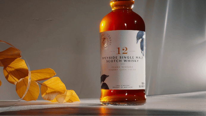 A bottle of 12-year-old Speyside single malt Scotch whisky on a surface next to yellow autumn leaves.