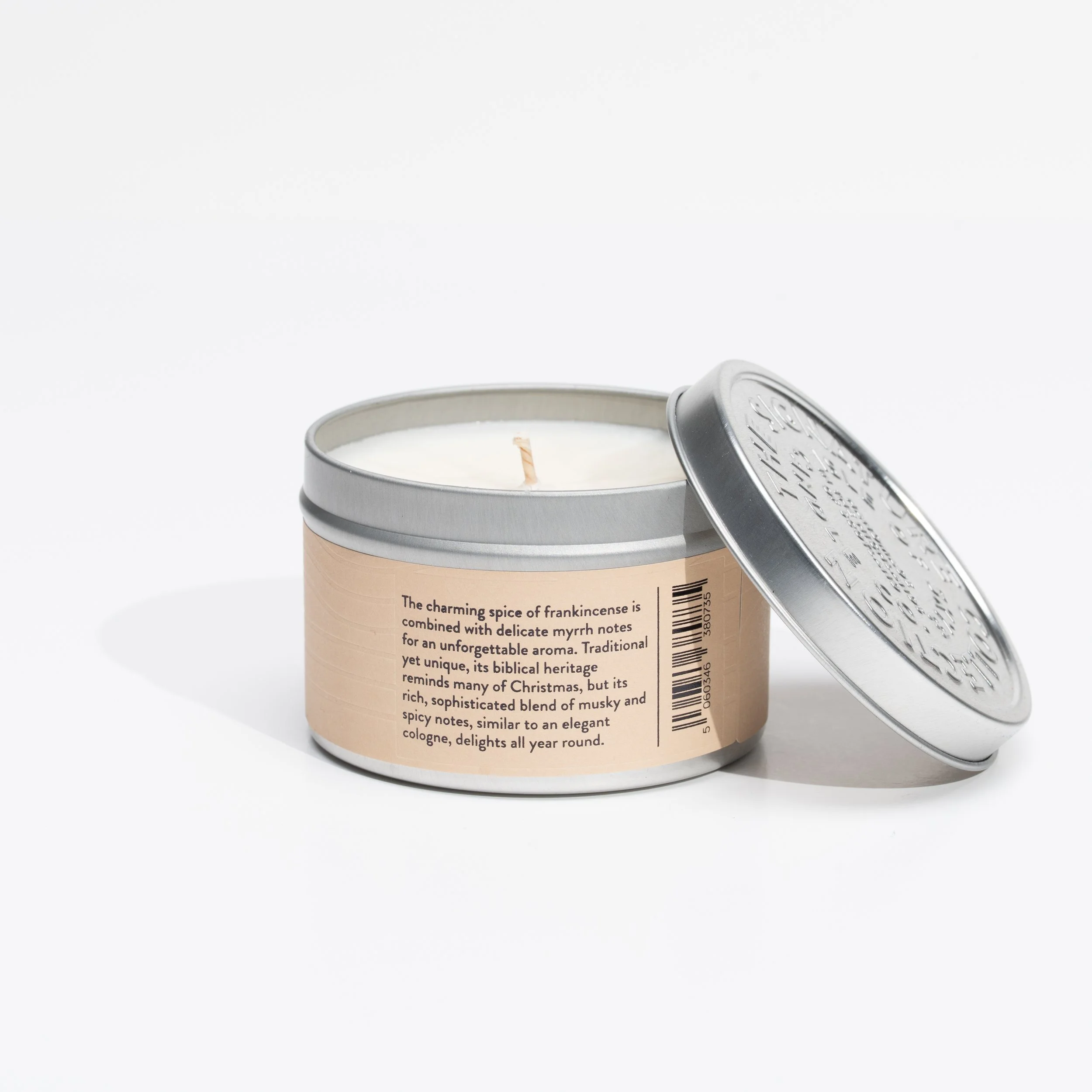 A scented candle in a round tin container with a silver lid, labeled with a description about frankincense scent and a barcode.