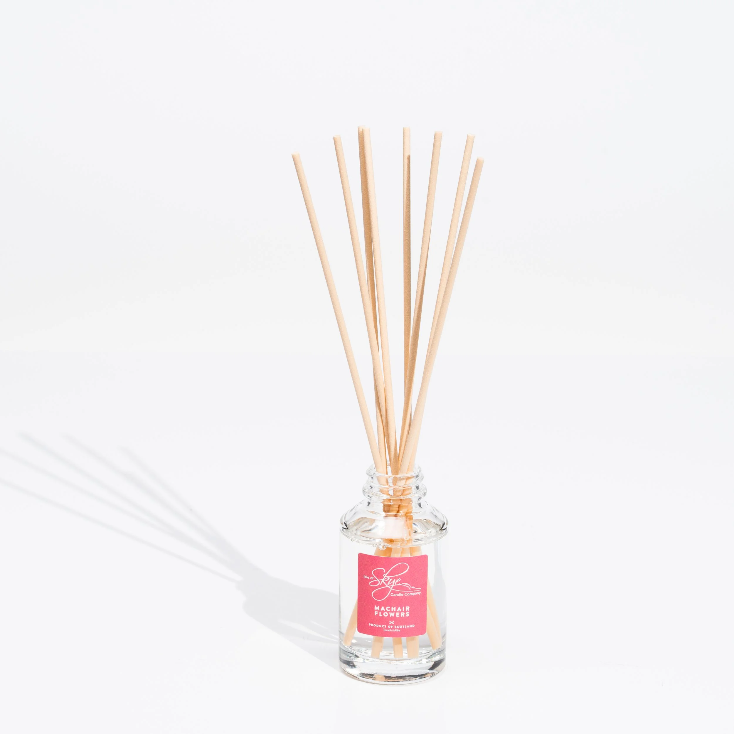 A glass jar on a white surface holding multiple reed sticks for a reed diffuser.