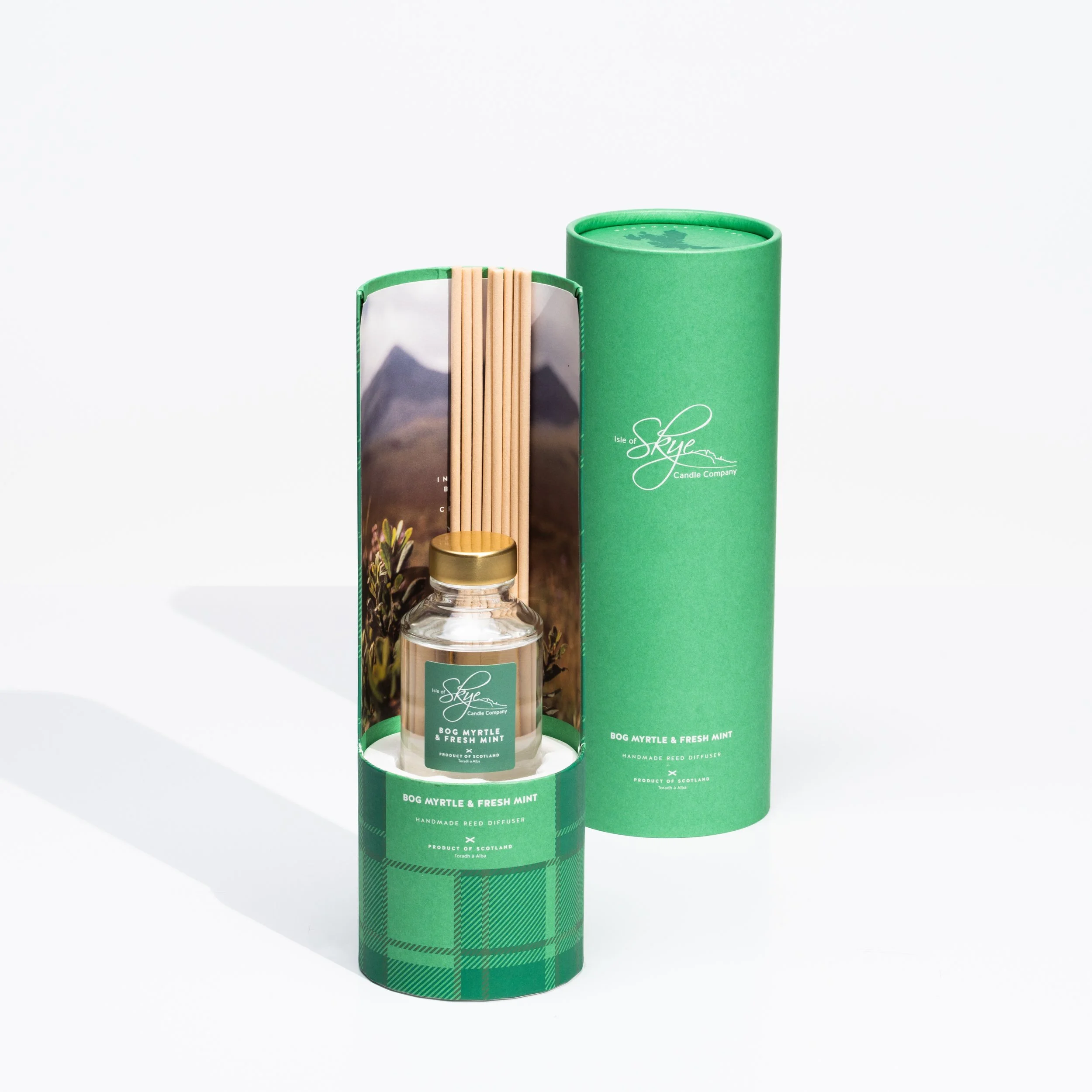 A glass reed diffuser with a gold top, labeled 'Bog Myrtle & Fresh Mint' from Isle of Skye Candle Company, next to a green cylindrical container with the same branding, on a white background.