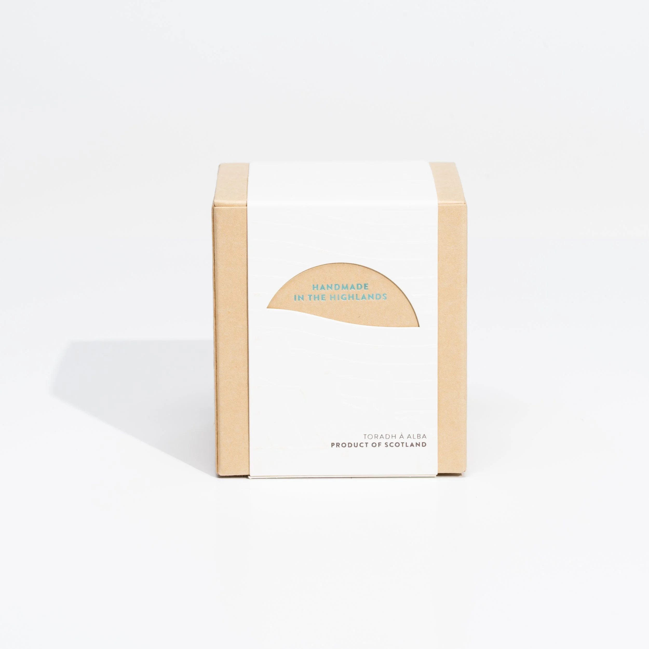 A cardboard box with a white label that has a semi-circular cutout revealing text 'Handmade in the Highlands' on a plain white background.