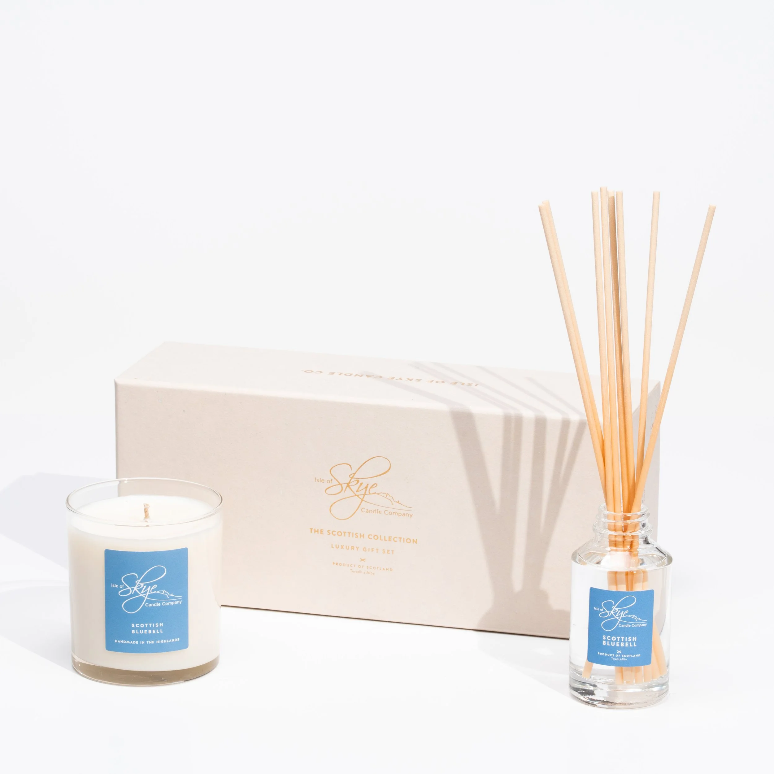 A luxury Scottish candle gift set including a white candle in a glass container and a reed diffuser with a glass bottle and wooden sticks, all branded with blue labels and a white box in the background.