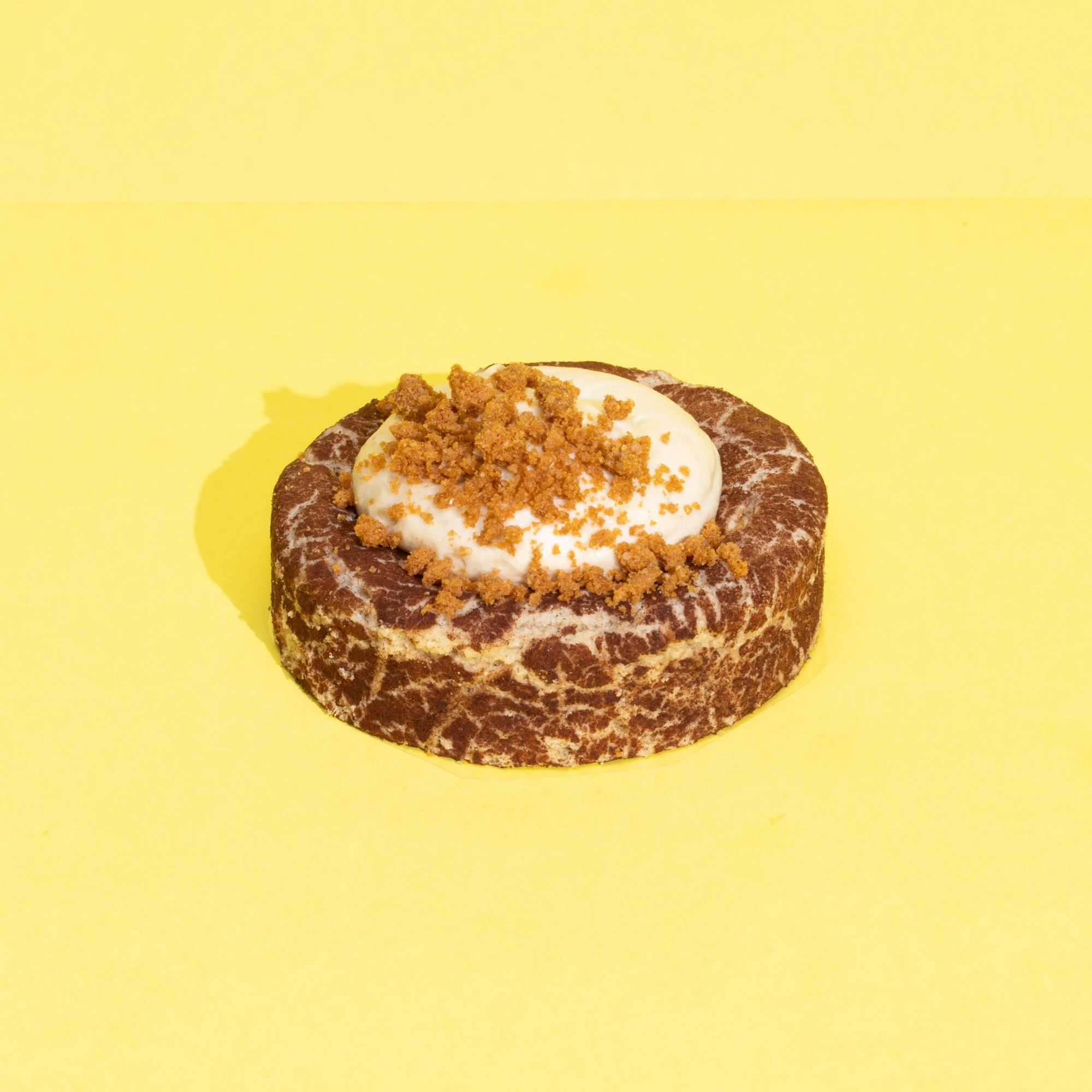 A dessert with a marble pattern, topped with whipped cream and crumbled cookies, on a yellow background.