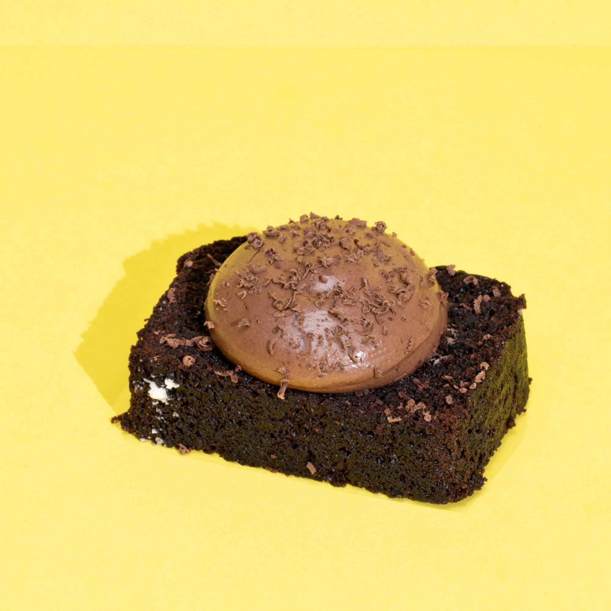 Chocolate dessert with a drizzle of caramel and chocolate shavings on top, served on a yellow background.