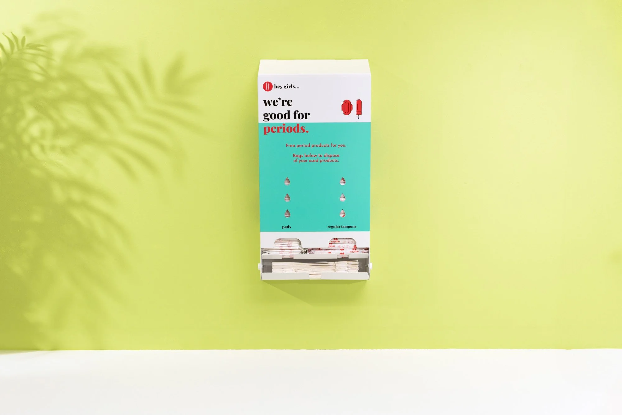 A periodic table-themed dispenser with pads and regular tampons against a yellow background, promoting menstrual products.