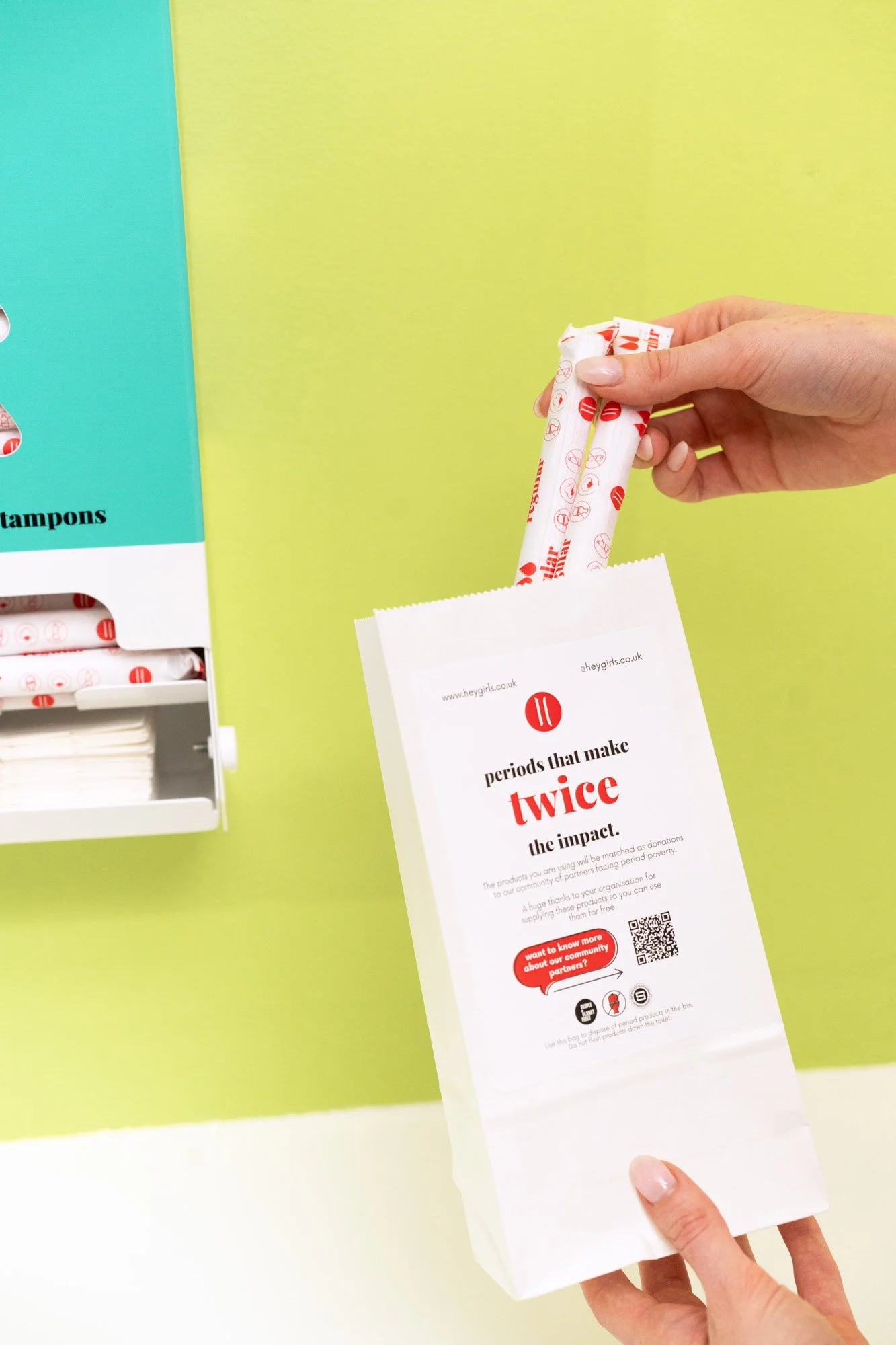 Person dropping menstrual pads from a paper bag into a waste bin with a green and yellow wall in the background.