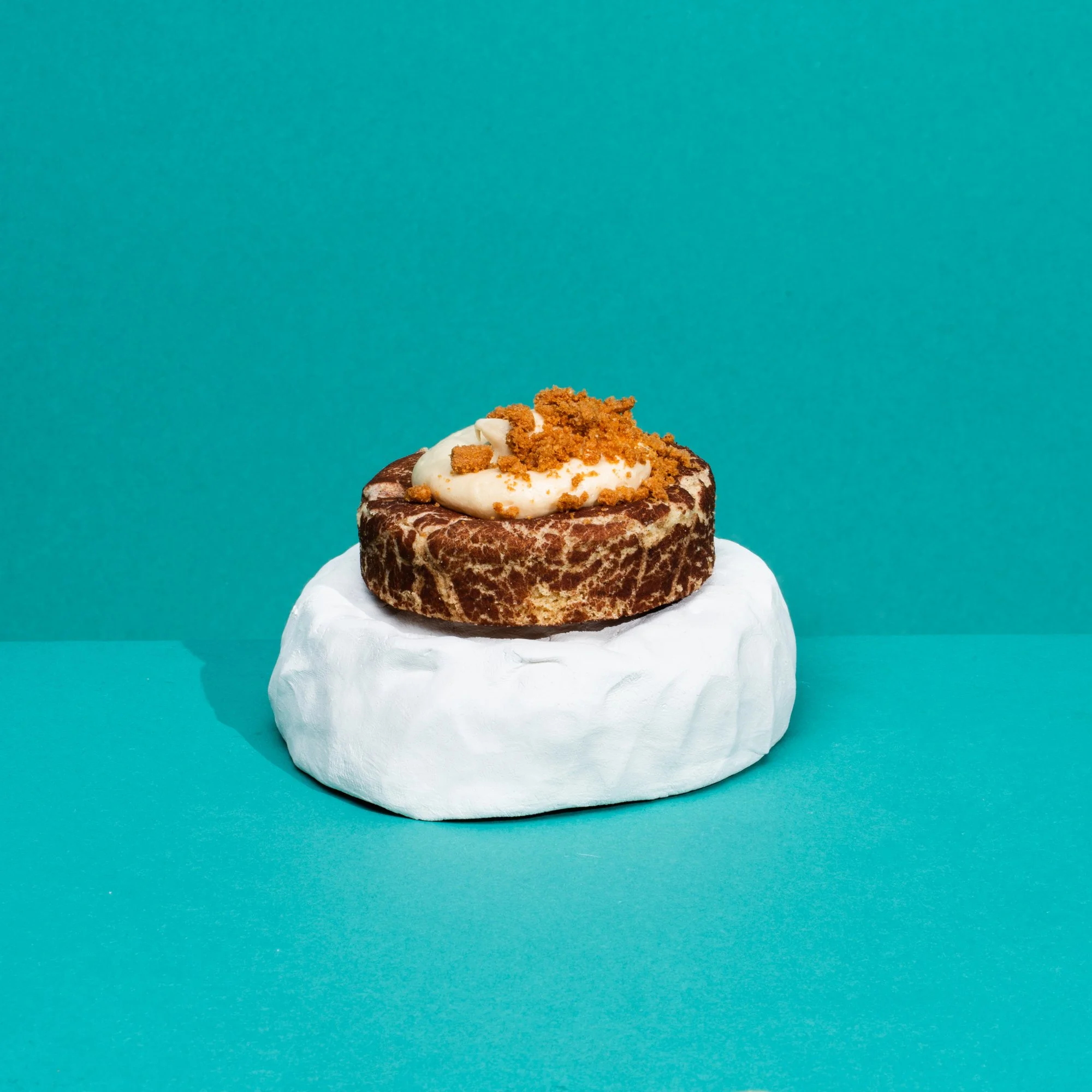 Sweet potato topped with whipped cream and crumbled cookie on a white object against a teal background.
