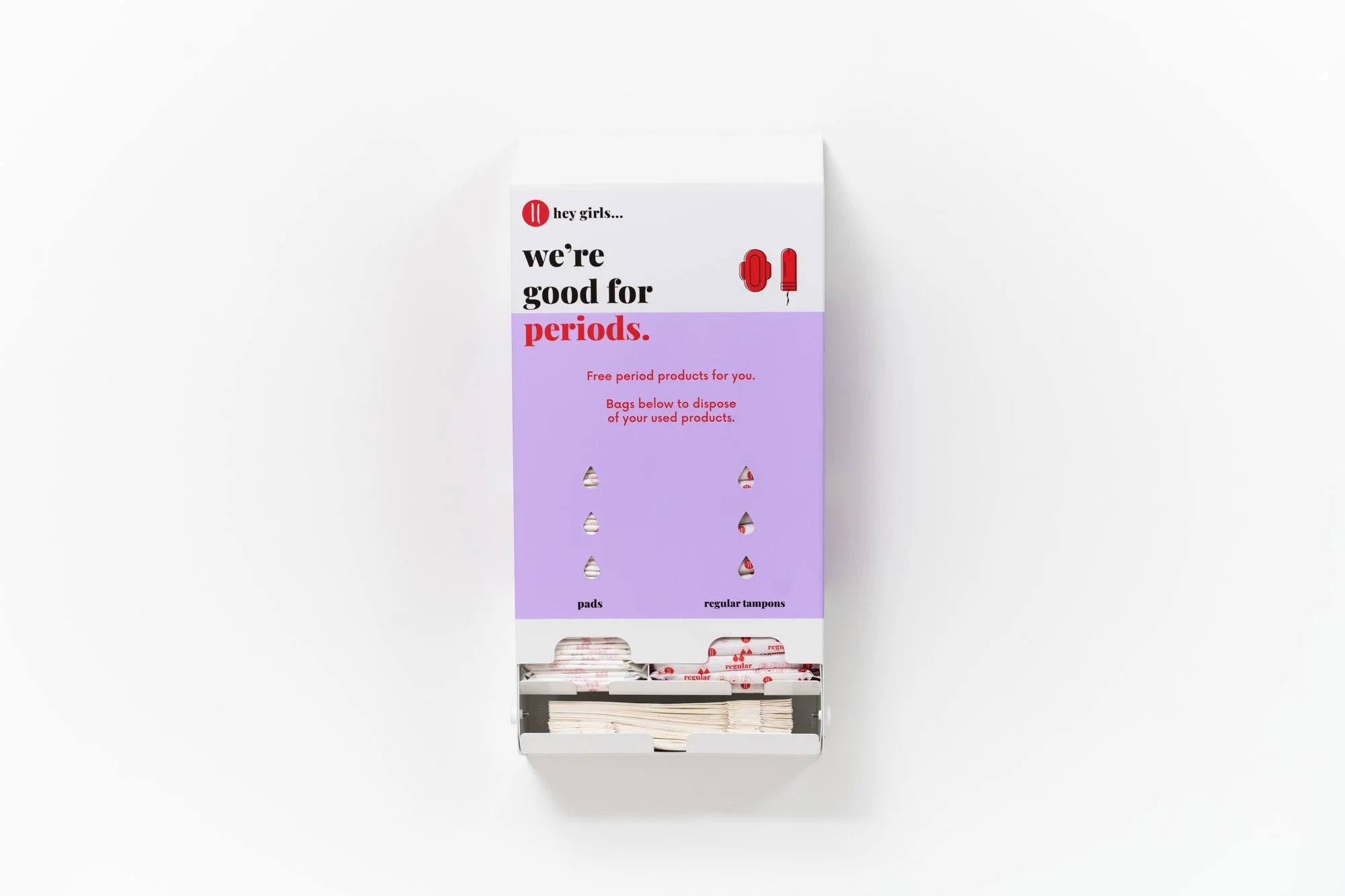 A white box with a purple section and red text that says 'we're good for periods.' Inside the box are various period products including pads and tampons, visible through small cut-out windows.