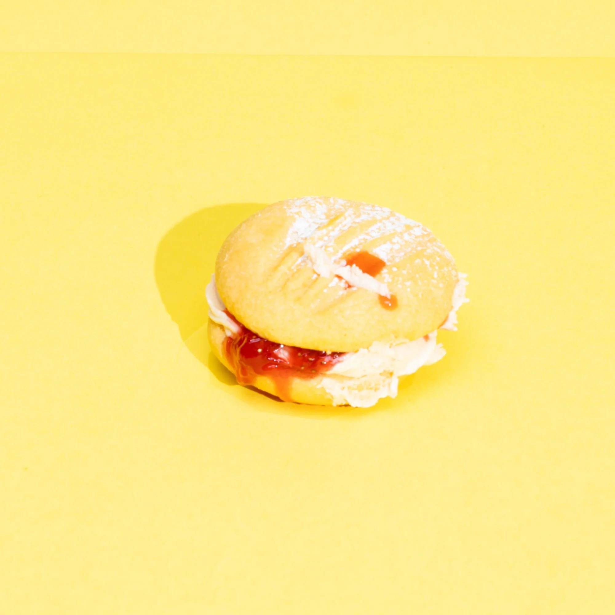 A partially eaten lemon-filled pastry with white icing on top, placed on a bright yellow background.