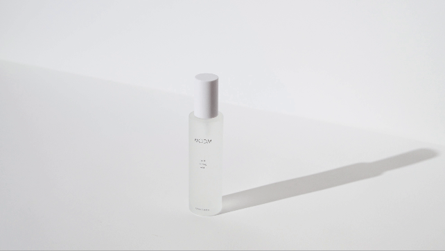 A white spray bottle standing on a white surface with a shadow to the right.