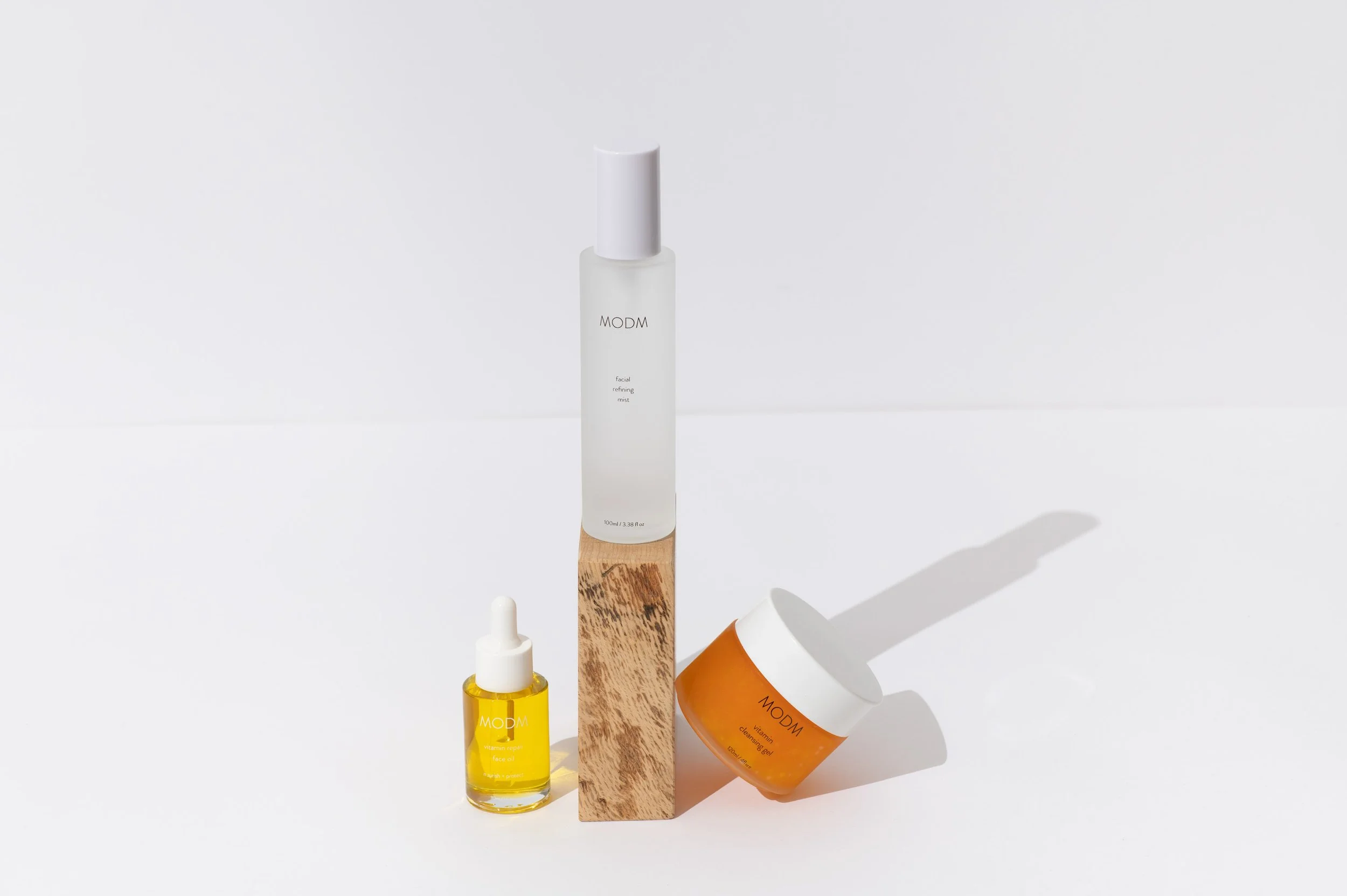 Skincare products from MODM including a yellow face oil, a facial refining mist, and a vitamin cleansing gel on a white background.