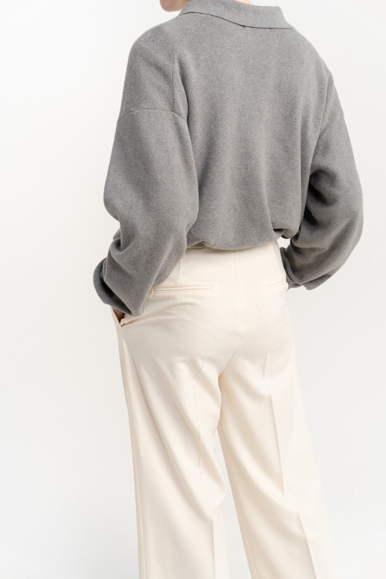 Person wearing a gray sweater and white high-waisted pants, seen from the back.