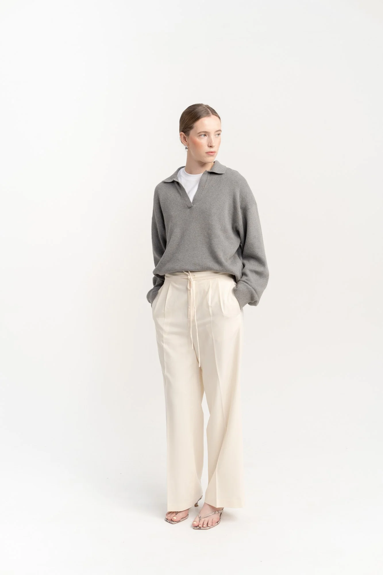 Woman wearing a gray pullover, white undershirt, and beige loose pants, standing against a plain white background.