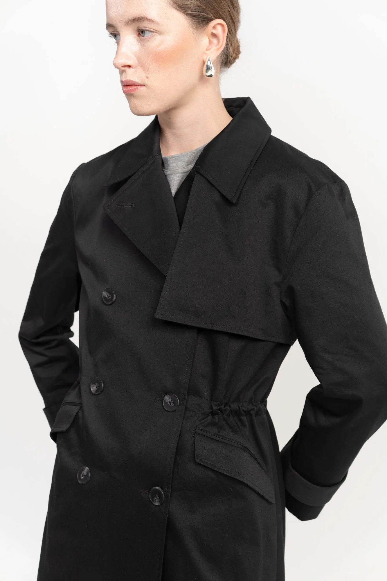 A woman wearing a black trench coat and teardrop-shaped earrings.