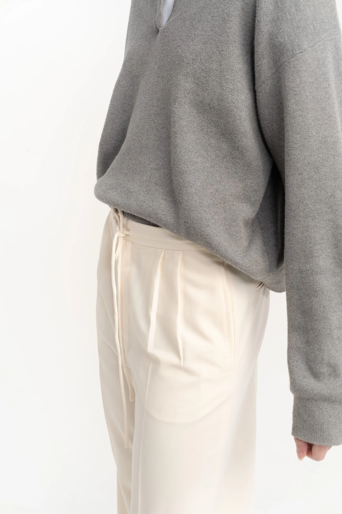 Person wearing a gray sweatshirt and cream-colored drawstring pants standing against a white background.