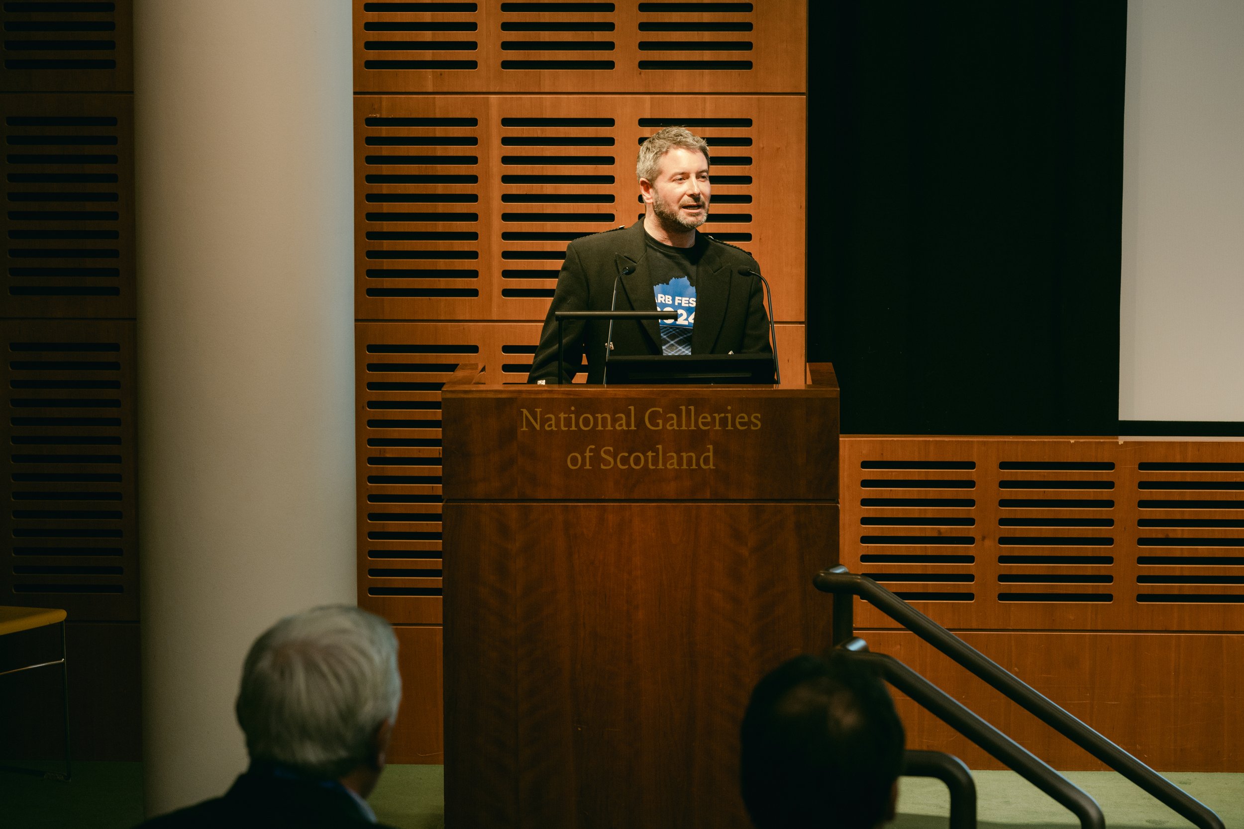A man giving a speech at a podium with the words "National Galleries of Scotland" in a conference room.