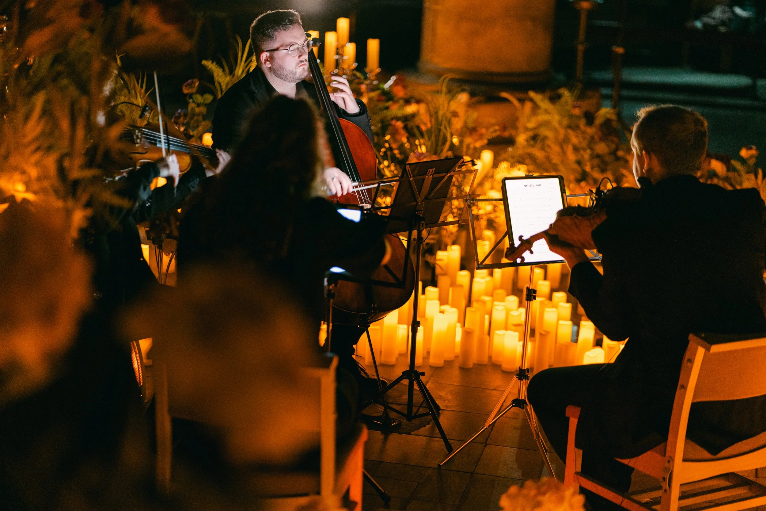 A string quartet performs at an evening event surrounded by lit candles and flowers, creating a warm and intimate atmosphere.