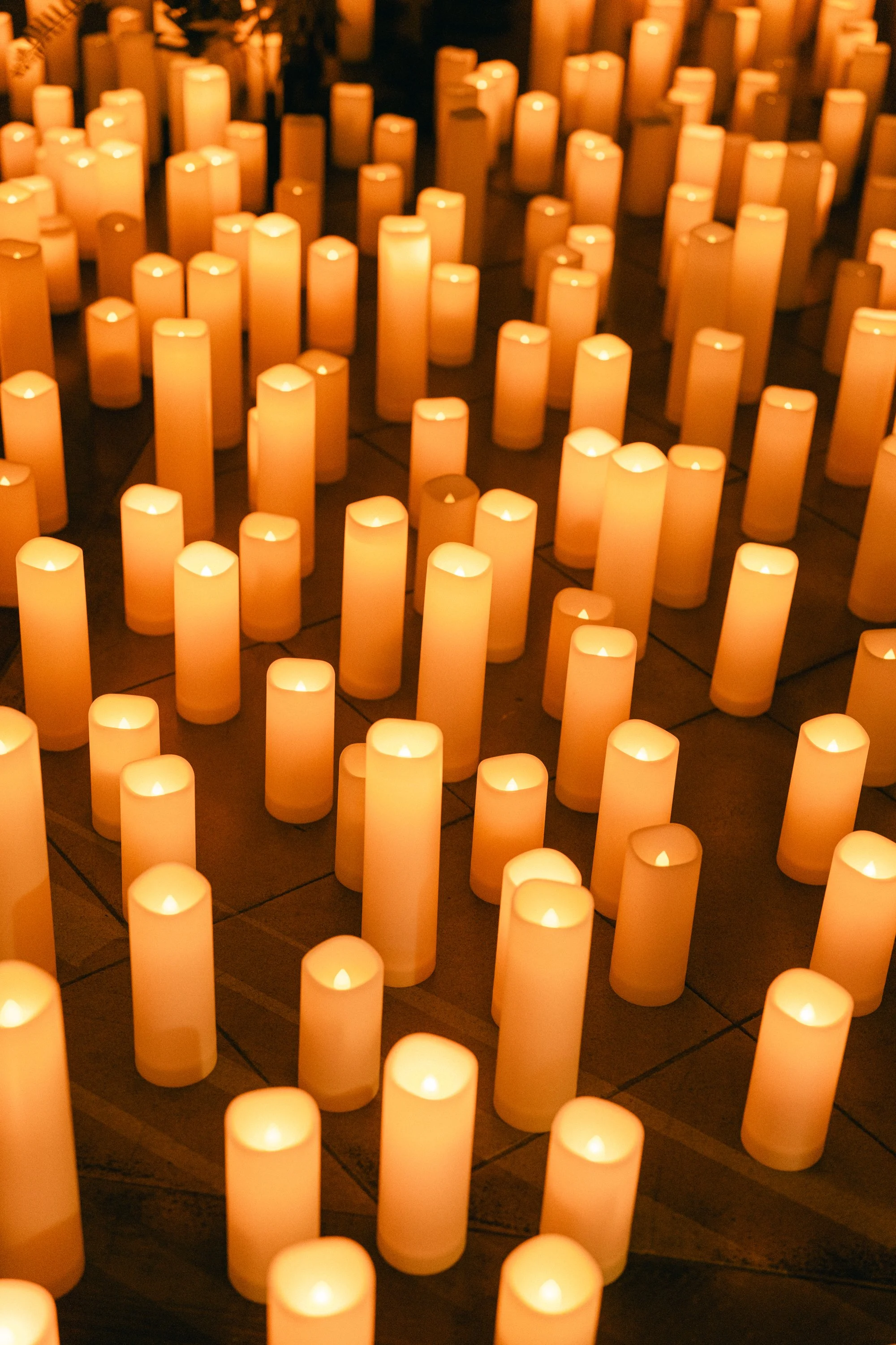 Rows of lit candles in white candle holders creating a warm glow.