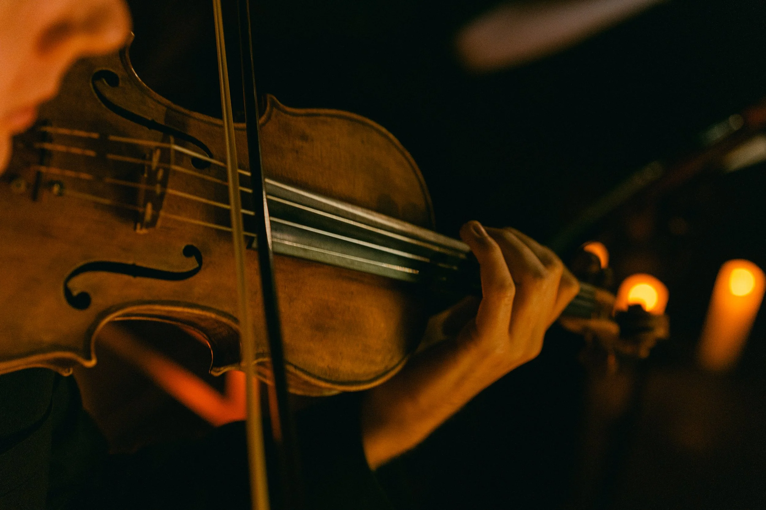 Close-up of a person playing a violin in a dimly lit setting with warm lighting.