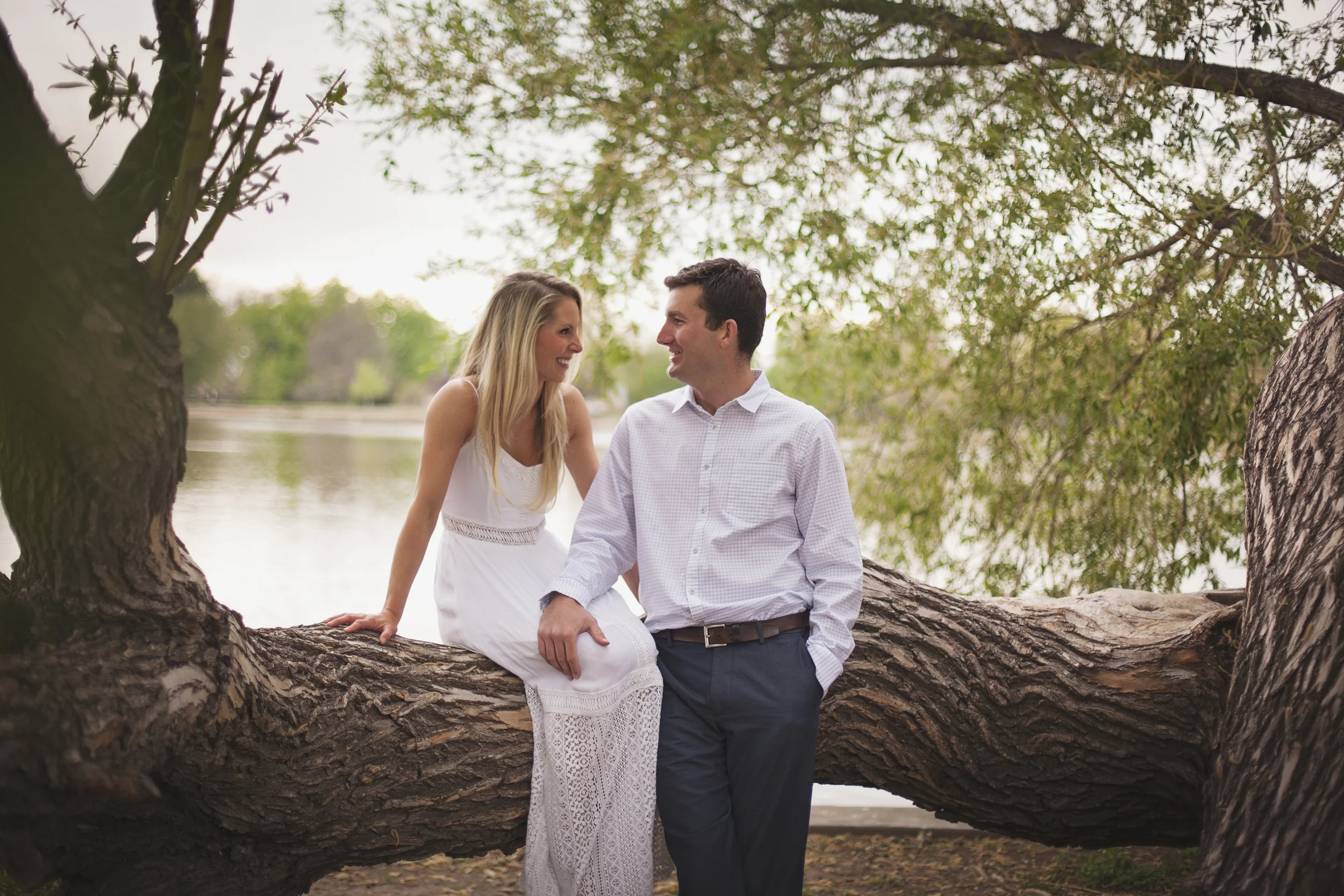 City Park engagement photography of engaged couple sitting on tree limb in front of lake