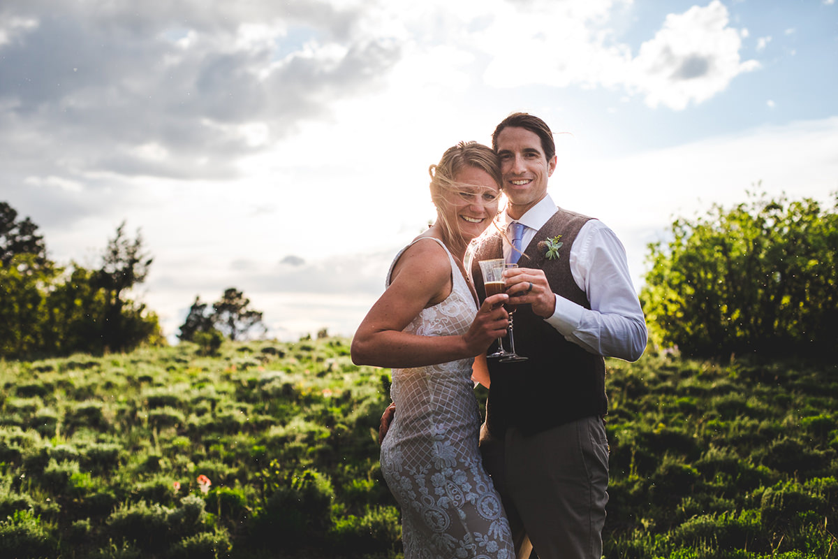 Bride and groom clinking glasses with sunset behind them