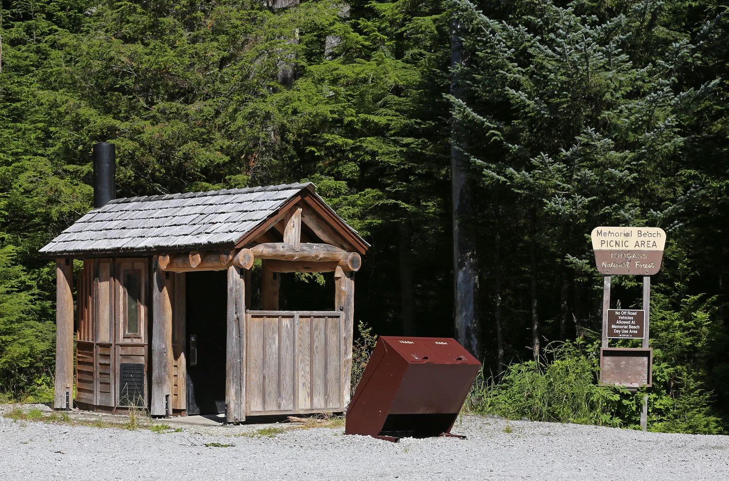 Parking lot and outhouse at Memorial Beach. In front of the outhouse are bear-proof trash cans. 