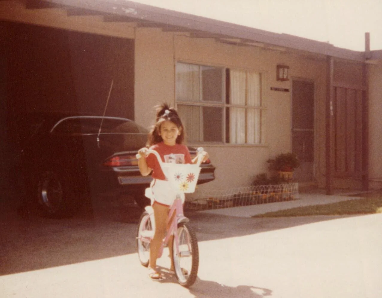 Child on pink bike in front of brown Camaro