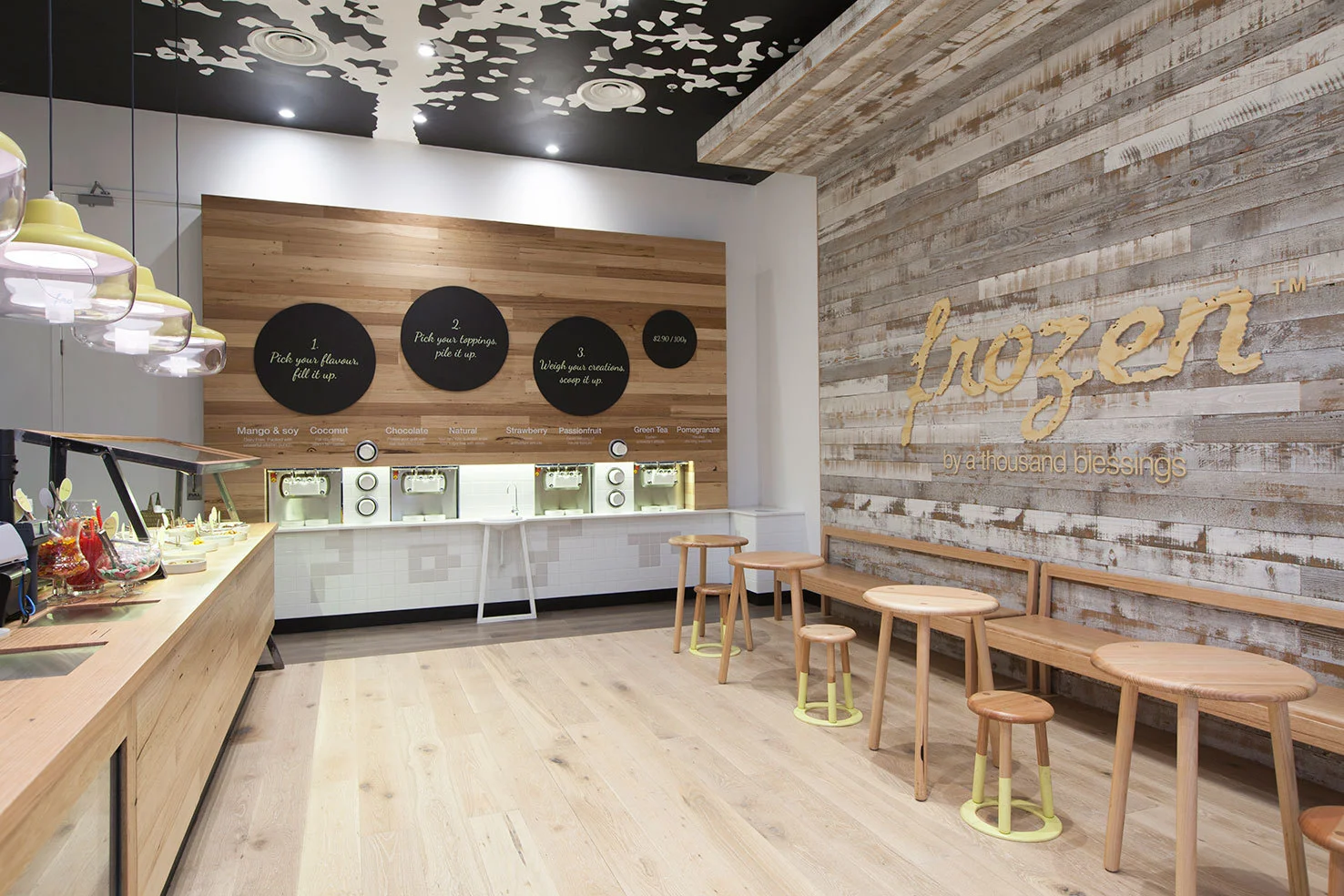 Frozen by a Thousand Blessings is a new self-serve frozen yoghurt concept store. Bought to you with love from the Thousand Blessings crew in Richmond, they provide biodynamic organic yoghurt with an ever changing list of freshly prepared toppings. The design response involves a simple palette of materials which allows the bright coloured toppings to stand out. Touches of yellow play add a playful element to the space. The great majority of timber used in the fitout is recycled, from the toppings counter, frozen yoghurt machine wall and the furniture, in an attempt to provide a sustainable and organic element to the space.The hand painted tree on the ceiling, designed by Pang & Haig, enhances the experience of the space. Doncaster Westfield was the first store designed by KVA for Frozen by a Thousand Blessings is part of their local roll out of stores. Stay tuned for more... Photography by Christine Wood Photographer