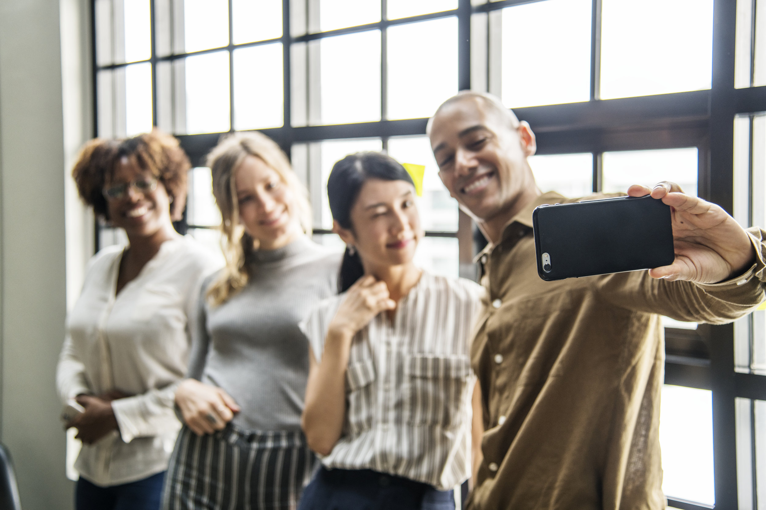A coloured man taking a selfie picture of others including asian and Caucasian people. We are all equal and your business should proudly display this.