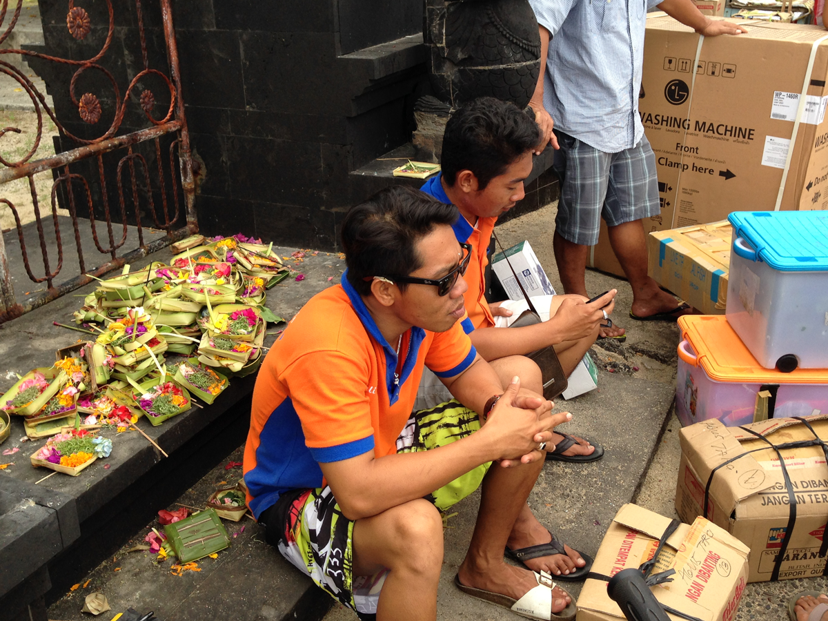 Daily life in Lembongan: Offerings in the background. Checking phones in the foreground.

