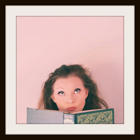 Blissom looks up from green book. Pink background in a frame. | The Naked Page