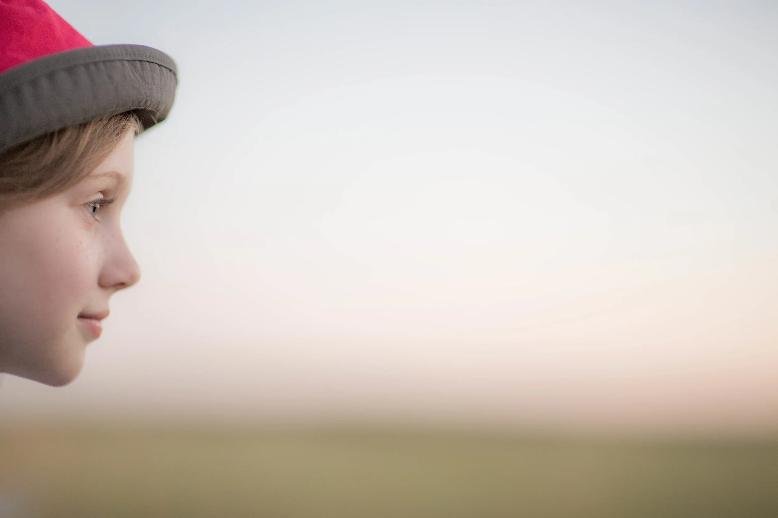 Profile of a child in a red knit hat looking out at a soft sunset sky, Alberta family travel photography (Copy)
