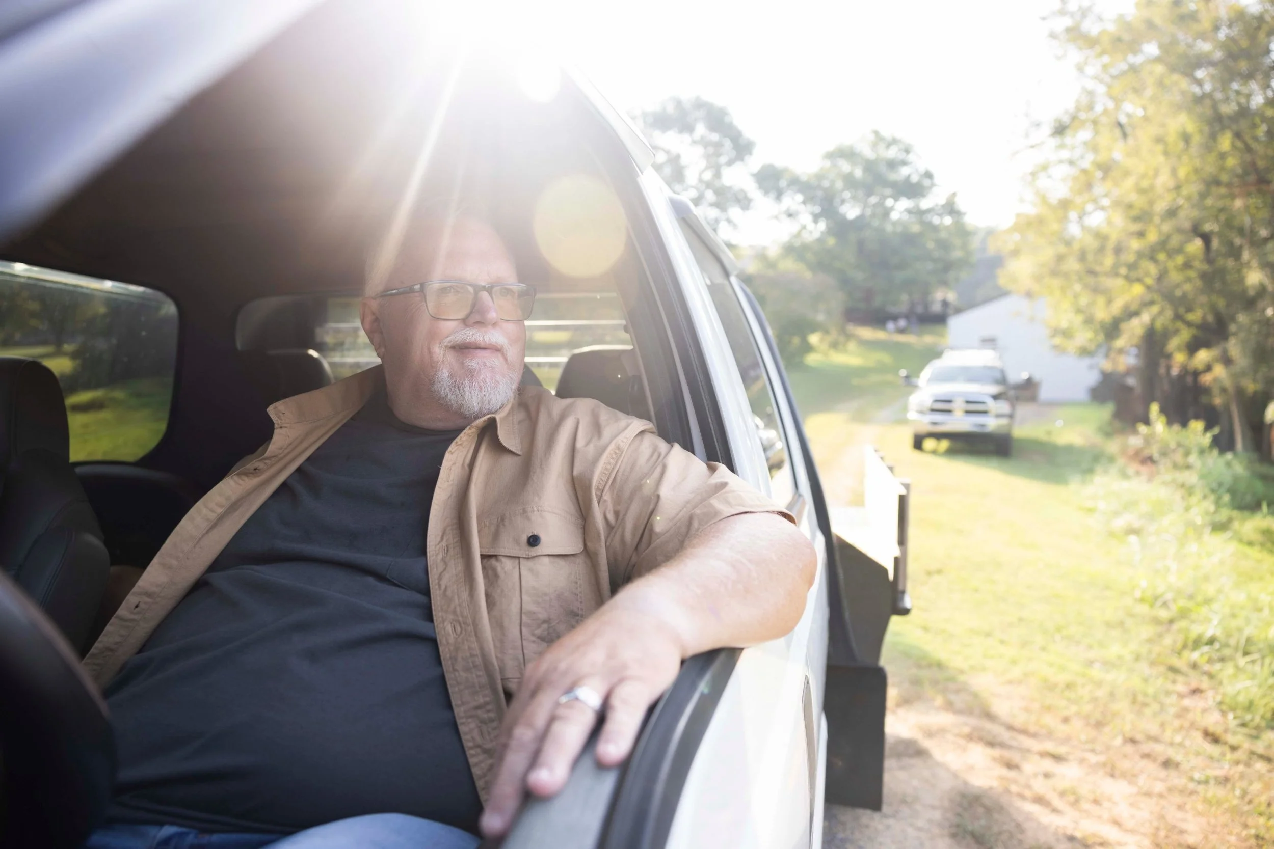 Patient portrait for a pharma campaign: man looking out the open door of a white truck in backlit morning sun