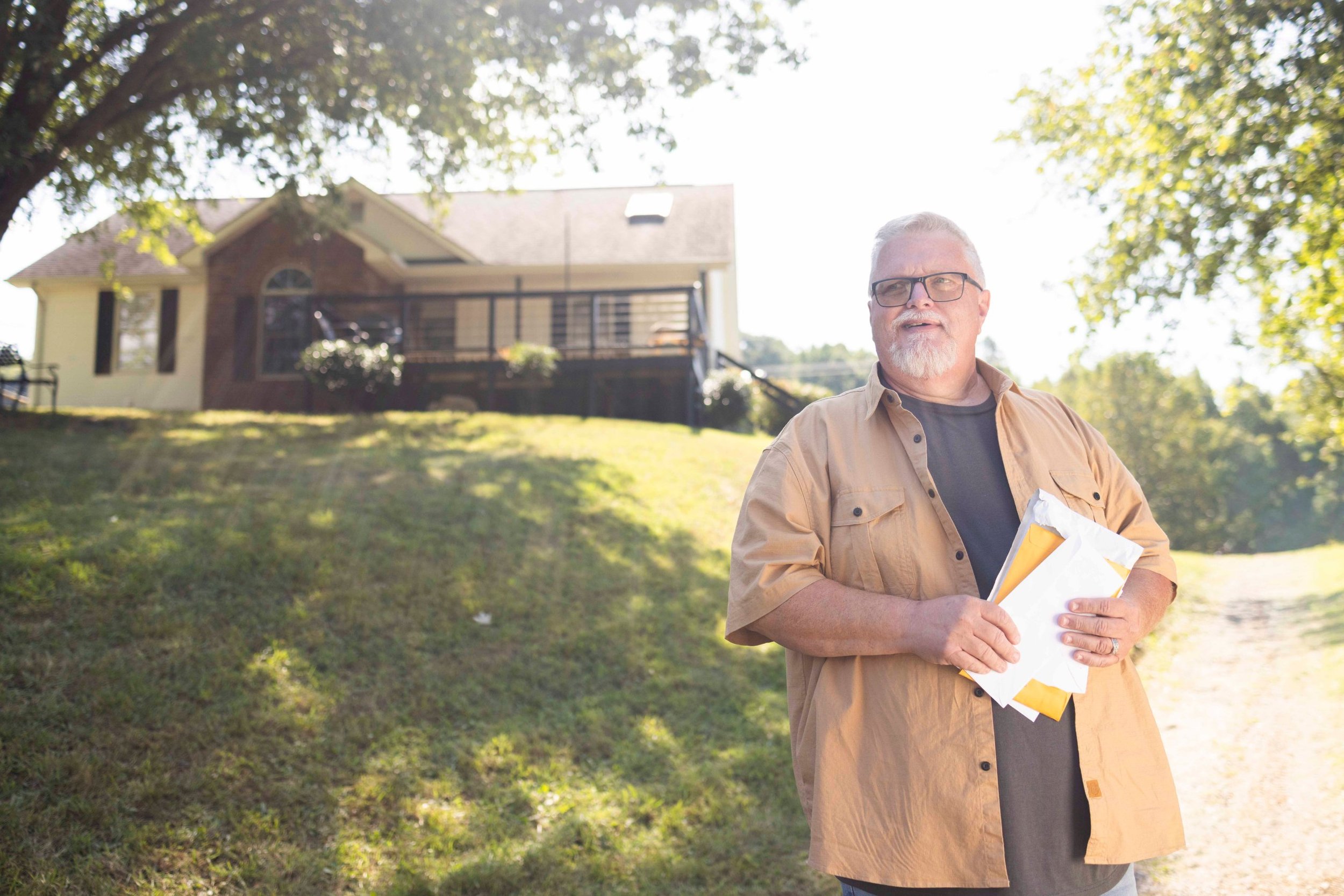 Pharma patient lifestyle photography: man holding mail in front of his house on a sunny day